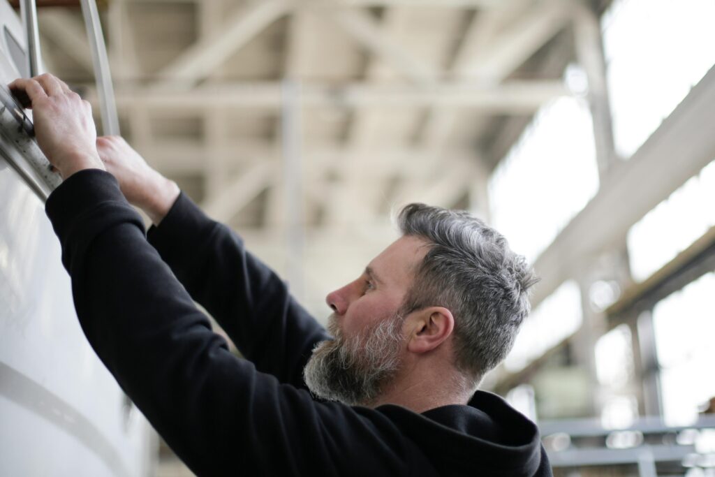 Side view of adult bearded mechanic in black workwear checking metal details while working in spacious modern hangar