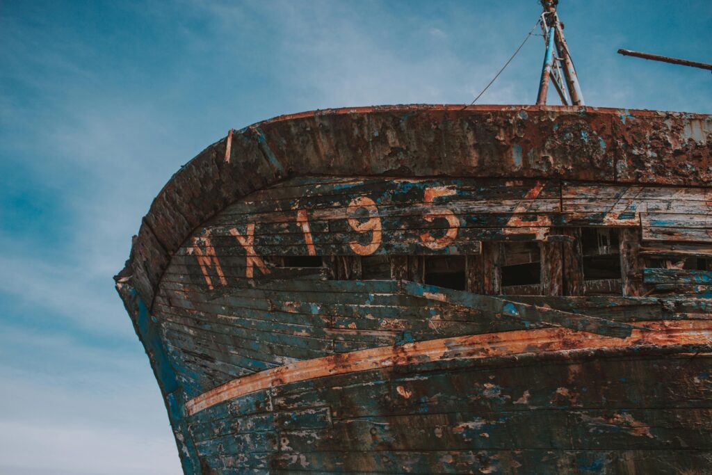 Low angle of detail of shabby abandoned ship located on shore against blue sky